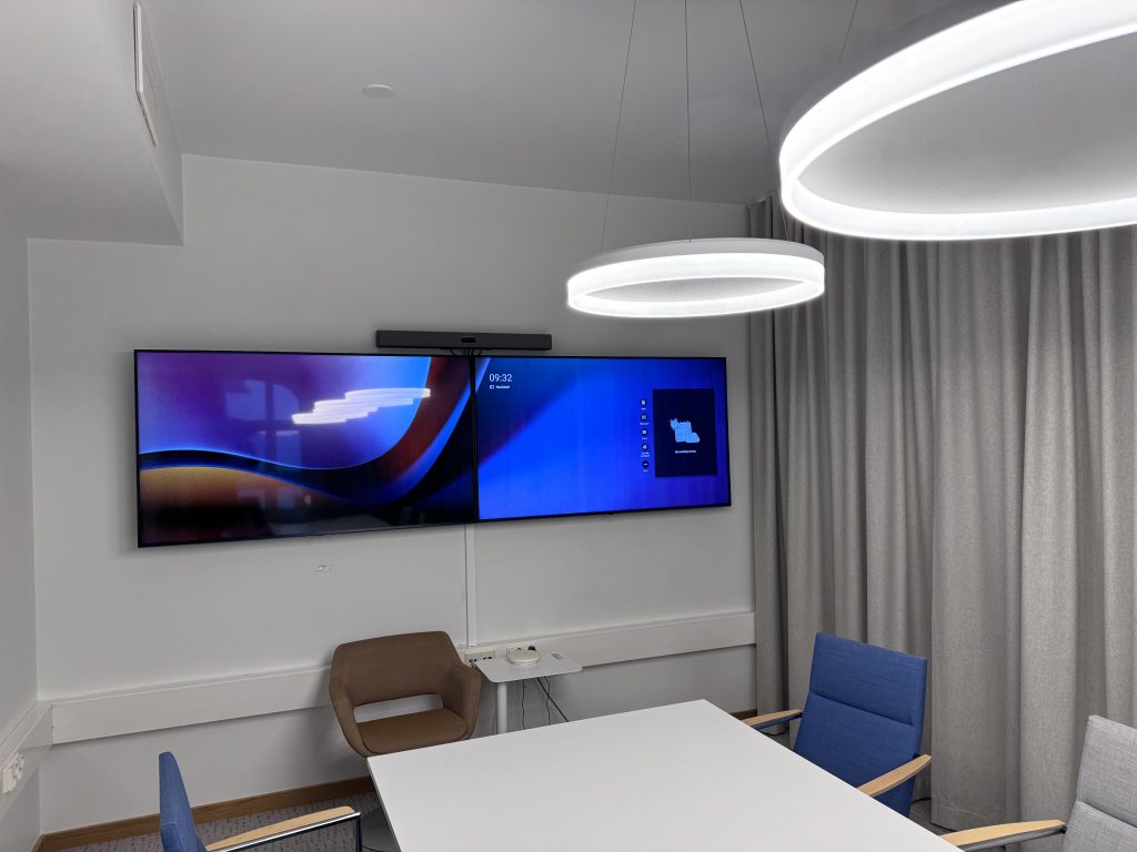 Neuvotteluhuoneen seinälle asennetut Neatbar Pro videoneuvottelujärjestelmä ja kaksi LG-näyttöä.